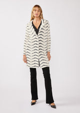 [Color: Cream/Black] A full body front facing image of a blonde model wearing a soft and fuzzy sweater coat in a white and black chevron design. With a snap button front, side pockets, and a classic notched lapel.