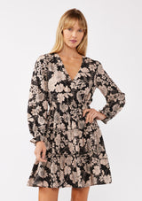 [Color: Black/Taupe] A front-facing image of a blonde model wearing a black and taupe floral print mini dress. This casual boho style features a surplice v-neckline, long sleeves with ruffled cuffs, and a flowy tiered skirt. Ideal for casual brunch outings, vacations, and special occasions.