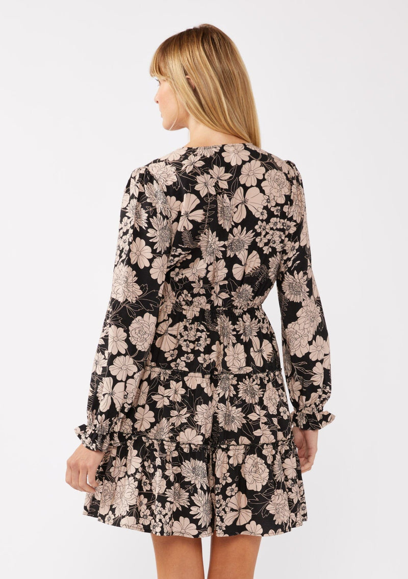 [Color: Black/Taupe] A back-facing image of a blonde model wearing a black and taupe floral print mini dress. This casual boho style features a surplice v-neckline, long sleeves with ruffled cuffs, and a flowy tiered skirt. Ideal for casual brunch outings, vacations, and special occasions.