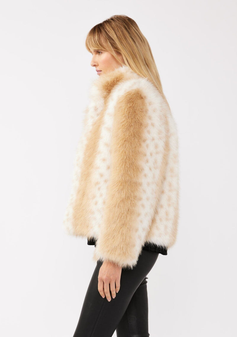 [Color: Natural] A side facing image of a blonde model wearing a tan brown stripe, dotted fur faux coat with an all black outfit. Featuring a high collar, open front, and long sleeves. A cold weather style, perfect for any special occasion. 