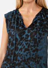 [Color: Midnight/Black] A detail image of a blonde model wearing a blue and black leopard print top. The top features a split V-neckline with tie detail, cap sleeves, and a relaxed silhouette. A versatile holiday top, ideal for both work and special occasions.