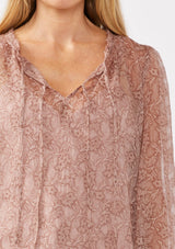 [Color: Mauve] A detail image of a blonde model wearing a crinkled sheer chiffon blouse with a floral pattern. This relaxed fit blouse features a double tie neck detail, long sleeves with ruffled elastic cuffs, and a detachable cami. 