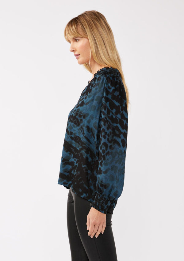 [Color: Midnight/Black] A side facing image of a blonde model wearing a leopard print blouse in black and blue. With a split v-neckline, smocked cuffs, and a smocked back detail. Ultra relaxed and flowy, perfect work and special occasions. 