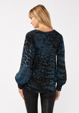 [Color: Midnight/Black] A back facing image of a blonde model wearing a leopard print blouse in black and blue. With a split v-neckline, smocked cuffs, and a smocked back detail. Ultra relaxed and flowy, perfect work and special occasions. 