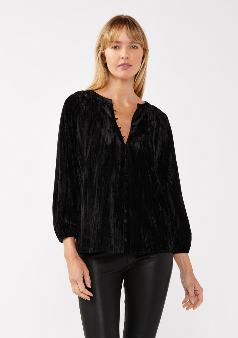 [Color: Black ] A front facing image of a blonde model wearing a black velvet blouse with a loop button front, long sleeves, and elastic cuffs. The boho-inspired holiday blouse is paired with black faux leather bottoms for a chic nighttime look.