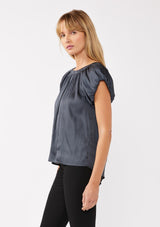 [Color: Midnight] A blonde model wearing a silky satin puff sleeve top with a round shirred neckline and a keyhole back with tie closure. The blue grey satin top is elegantly draped and polished, perfect for festive gatherings and special occasions.