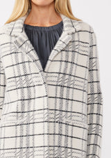 [Color: Cream/Black] A detail image of a blonde model wearing a fuzzy statement sweater coat in a cream and black plaid print. With long sleeves, a notched collar, a snap button front, and side patch pockets. 