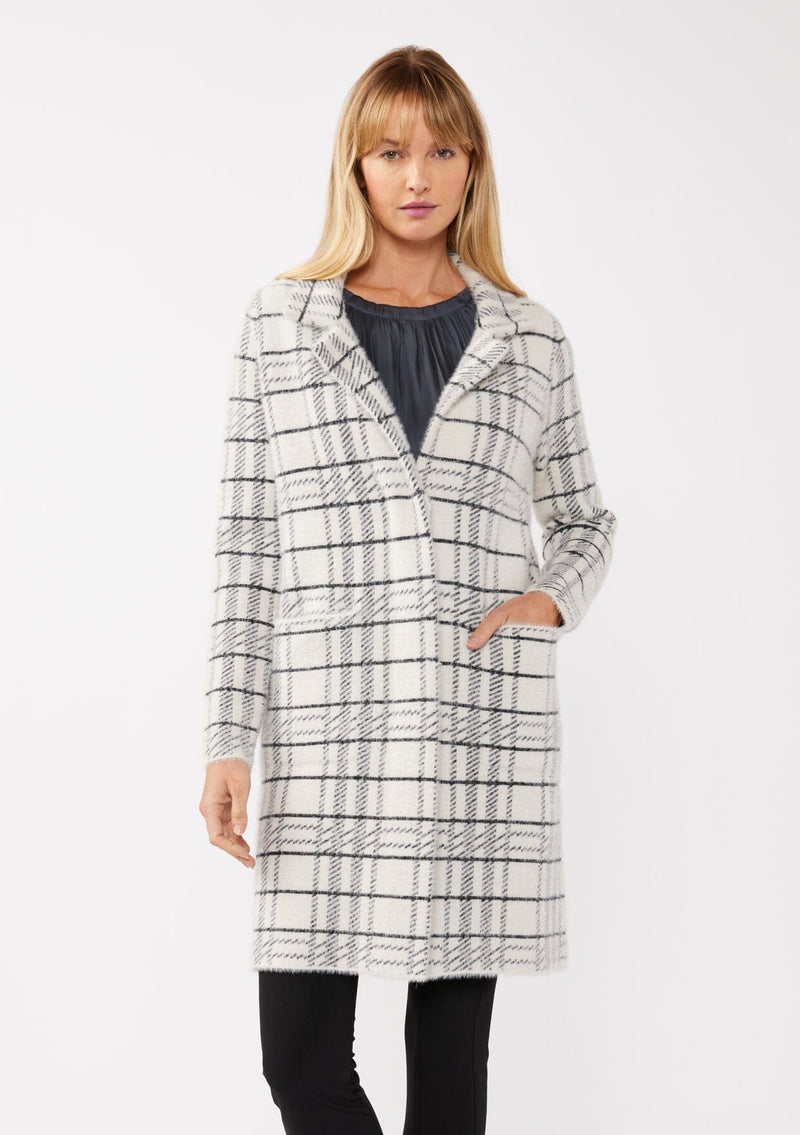 [Color: Cream/Black] A front facing image of a blonde model wearing a fuzzy statement sweater coat in a cream and black plaid print. With long sleeves, a notched collar, a snap button front, and side patch pockets. 