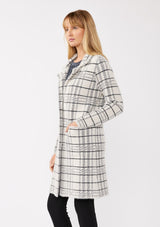 [Color: Cream/Black] A side facing image of a blonde model wearing a fuzzy statement sweater coat in a cream and black plaid print. With long sleeves, a notched collar, a snap button front, and side patch pockets. 