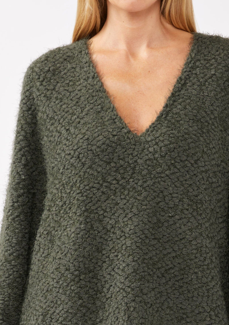 [Color: Olive] A detail image of a blonde model wearing a green cozy, fuzzy popcorn-textured pullover sweater with long sleeves, a classic V-neckline, and a high-low hemline. Ideal for lounging or casual fall outings.