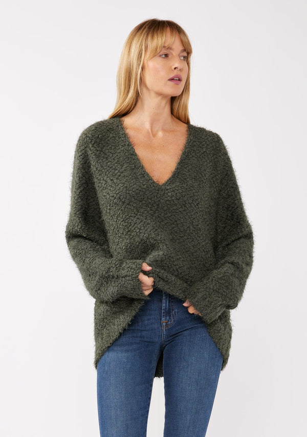 [Color: Olive] A front-facing image of a blonde model wearing a green cozy, fuzzy popcorn-textured pullover sweater with long sleeves, a classic V-neckline, and a high-low hemline. Ideal for lounging or casual fall outings.