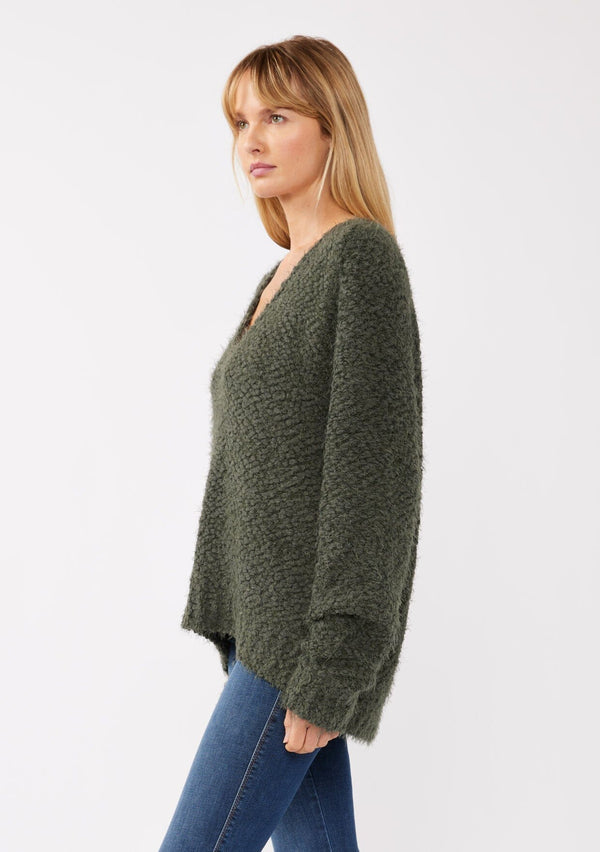 [Color: Olive] A side-facing image of a blonde model wearing a green cozy, fuzzy popcorn-textured pullover sweater with long sleeves, a classic V-neckline, and a high-low hemline. Ideal for lounging or casual fall outings.