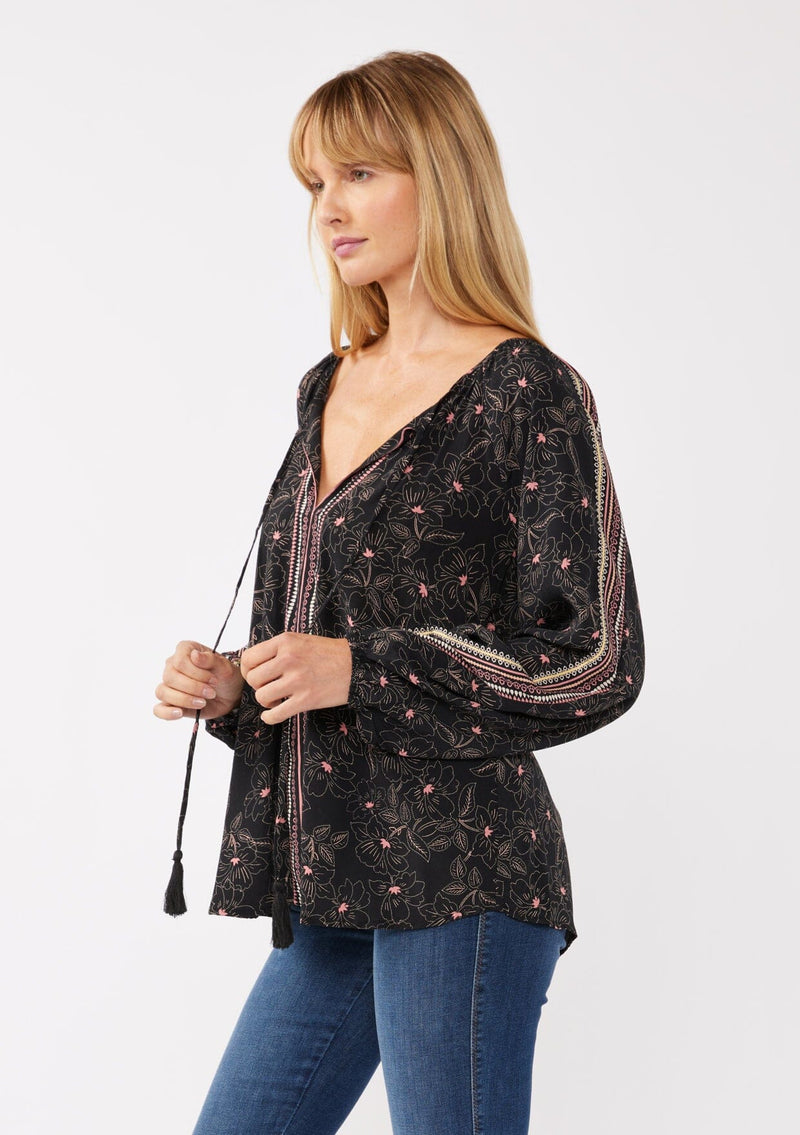 [Color: Black/Rose] A model wearing a classic black bohemian peasant top with romantic pink floral print. With long voluminous sleeves and a split v neckline with tassel ties. 