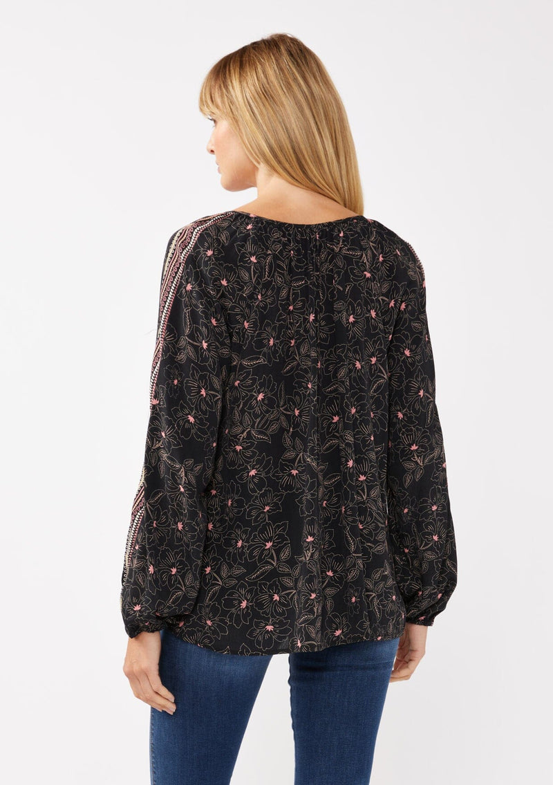 [Color: Black/Rose] A model wearing a classic black bohemian peasant top with romantic pink floral print. With long voluminous sleeves and a split v neckline with tassel ties. 