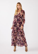 [Color: Plum/Dusty Rose] A full body front facing image of a blonde model wearing a sheer, empire waist maxi dress with a purple floral pattern. This flowy relaxed dress features a v-neckline, long sleeves, a button front, a ruffle cuff, and a tiered skirt. A fall special occasion dress for weddings, holiday events, and more. 