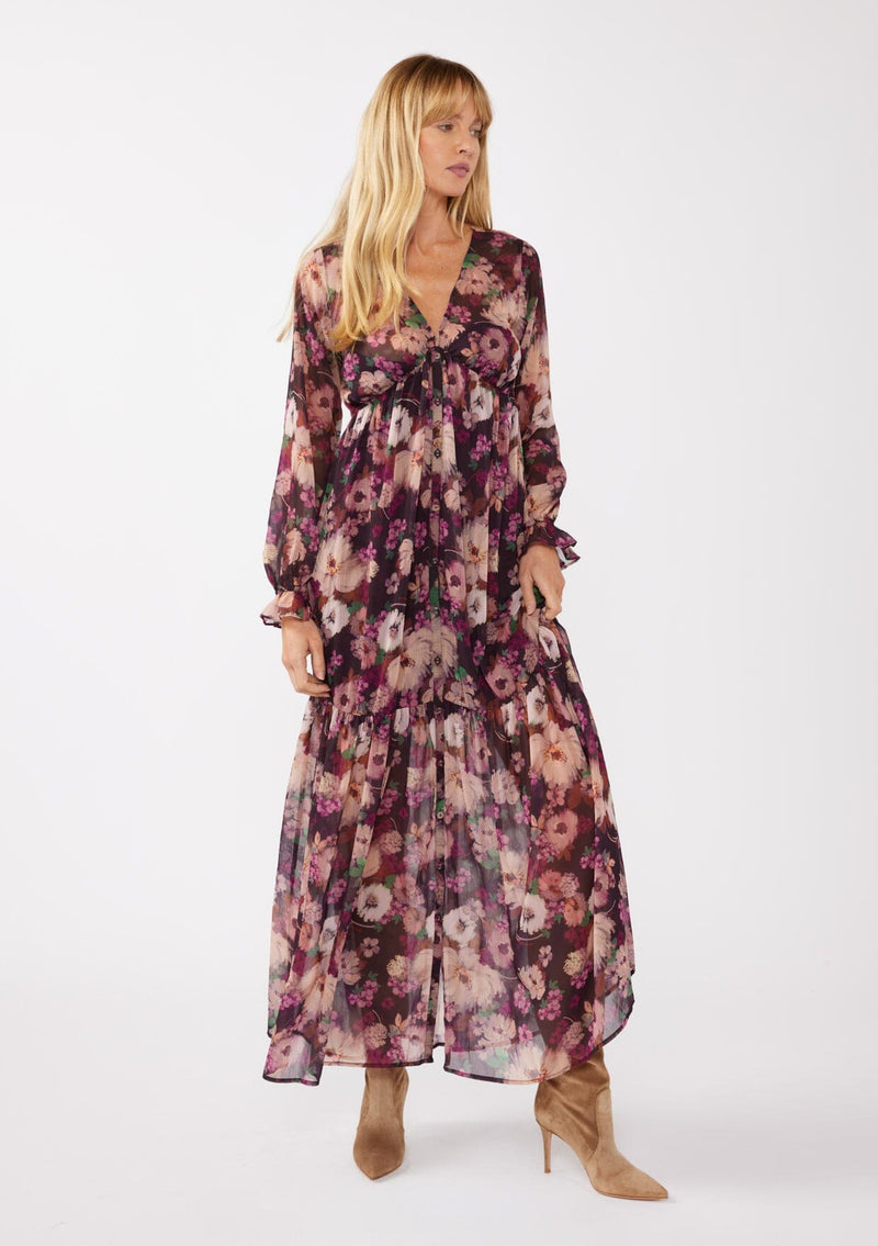 [Color: Plum/Dusty Rose] A full body front facing image of a blonde model wearing a sheer, empire waist maxi dress with a purple floral pattern. This flowy relaxed dress features a v-neckline, long sleeves, a button front, a ruffle cuff, and a tiered skirt. A fall special occasion dress for weddings, holiday events, and more. 