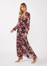 [Color: Plum/Dusty Rose] A full body side facing image of a blonde model wearing a sheer, empire waist maxi dress with a purple floral pattern. This flowy relaxed dress features a v-neckline, long sleeves, a button front, a ruffle cuff, and a tiered skirt. A fall special occasion dress for weddings, holiday events, and more. 