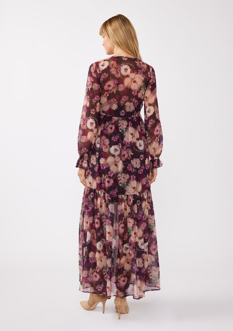 [Color: Plum/Dusty Rose] A full body back facing image of a blonde model wearing a sheer, empire waist maxi dress with a purple floral pattern. This flowy relaxed dress features a v-neckline, long sleeves, a ruffle cuff, and a tiered skirt. A fall special occasion dress for weddings, holiday events, and more. 