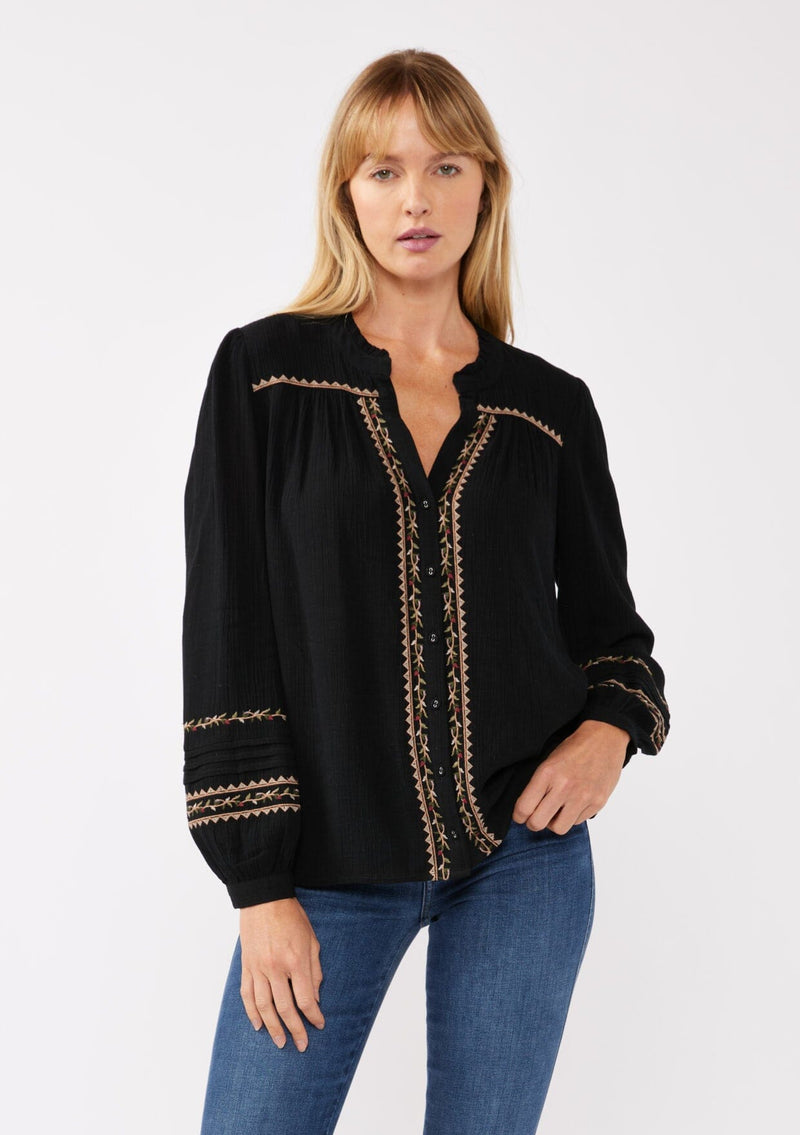 [Color: Black/Mocha] A front facing image of a blonde model wearing a black button-front blouse with contrasting embroidered details throughout. The boho blouse features a relaxed fit, long sleeves, a split V-neckline, and button-cuff closures. Styled with denim for the perfect fall ensemble. 