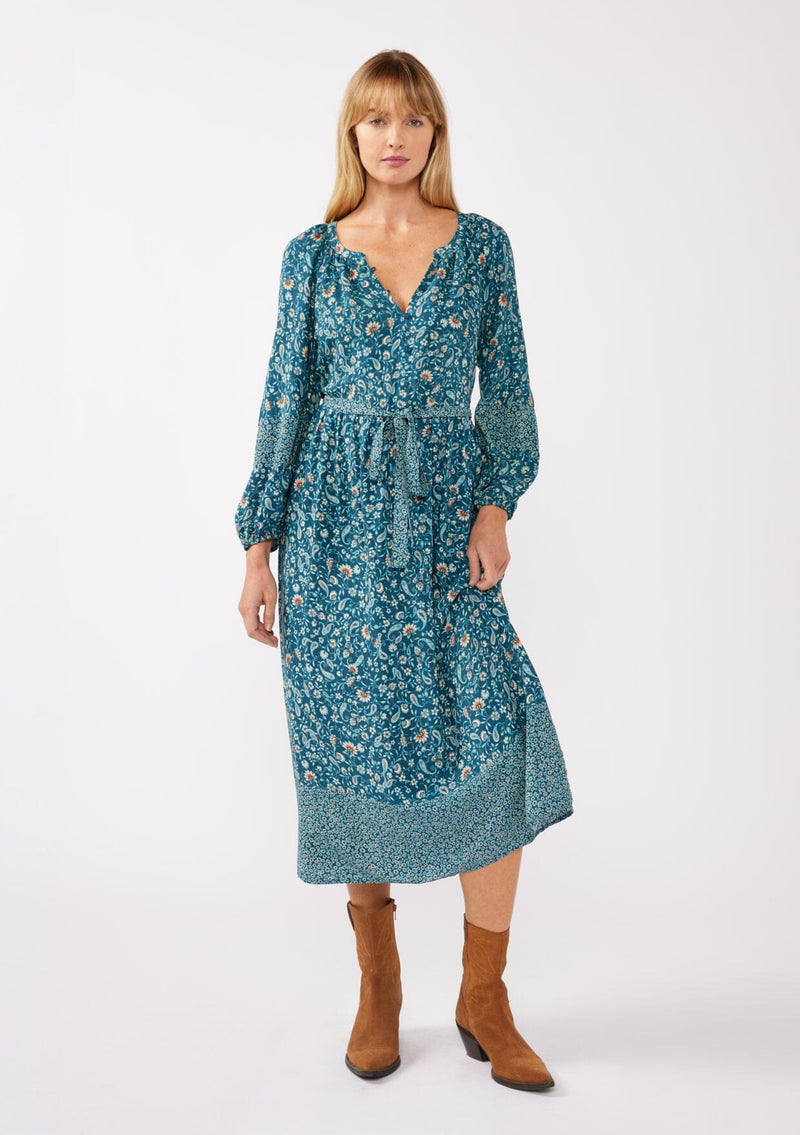 [Color: Teal/Cream] A full body image of a blonde model wearing an all-over teal floral print midi dress. The dress features long sleeves, a button-front, a self-tie waist belt, and a straight hem. Styled with brown boots, it highlights a relaxed silhouette and effortless elegance.