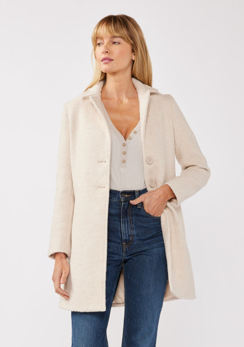 [Color: Natural/Sand] A front facing image of a blonde model wearing classic mid length coat in off white. This chevron textured coat features a classic notched lapel, a button front, and side pockets. A closet staple for the fall and winter season. 