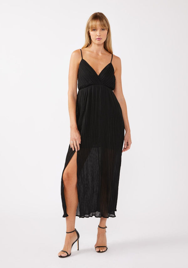 [Color: Black] A blonde model wearing a sleeveless, pleated maxi dress with heels. This special occasion dress features a surplice v neckline, empire waistline, an adjustable strappy back, and a side slit. Perfect for the holidays or any special event. 