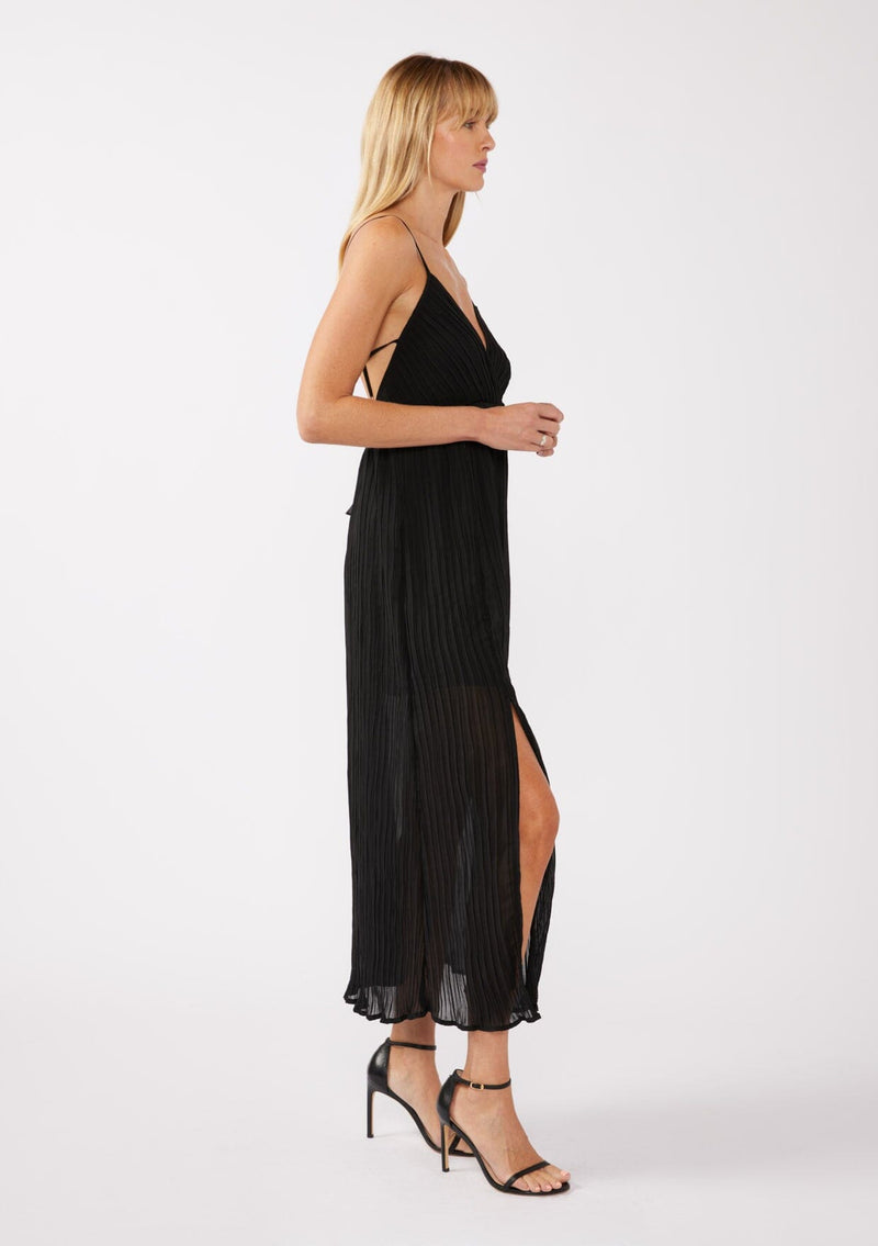 [Color: Black] A side facing image of a blonde model wearing a sleeveless, pleated maxi dress with heels. This special occasion dress features a surplice v neckline, empire waistline, an adjustable strappy back, and a side slit. Perfect for the holidays or any special event. 