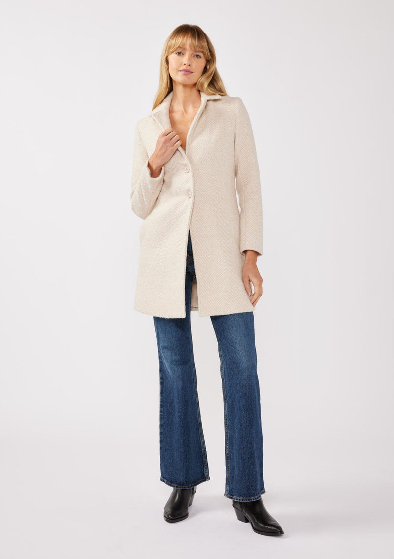 [Color: Natural/Sand] A full body front facing image of a blonde model wearing classic mid length coat in off white. This chevron textured coat features a classic notched lapel, a button front, and side pockets. A closet staple for the fall and winter season. 