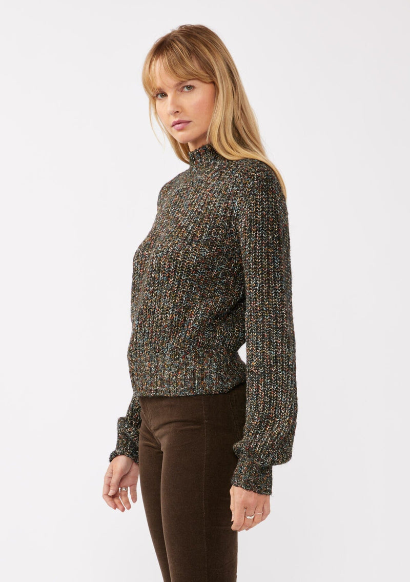 [Color: Black Multi] A side facing image of a blonde model wearing a chunky multi color knit sweater with a mock neckline and long voluminous sleeves. 