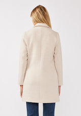 [Color: Natural/Sand] A back facing image of a blonde model wearing classic mid length coat in off white. This chevron textured coat features a classic notched lapel, a button front, and side pockets. A closet staple for the fall and winter season. 