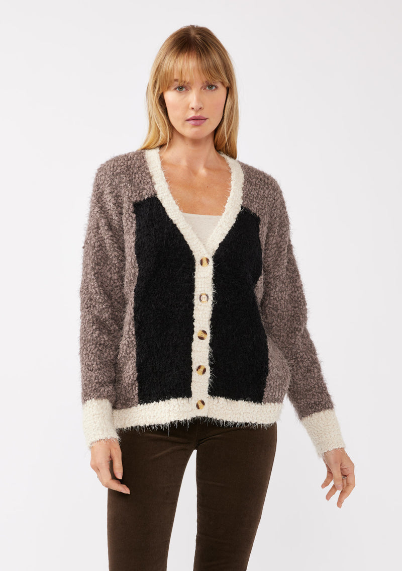 [Color: Vanilla Black] A front facing image of a blonde model wearing an ultra warm color block cardigan in a soft fuzzy popcorn texture. Featuring a classic tortoiseshell button up front, a flattering v neckline, and a contrast trim. This fuzzy cardigan is perfect for layering during the fall season. 