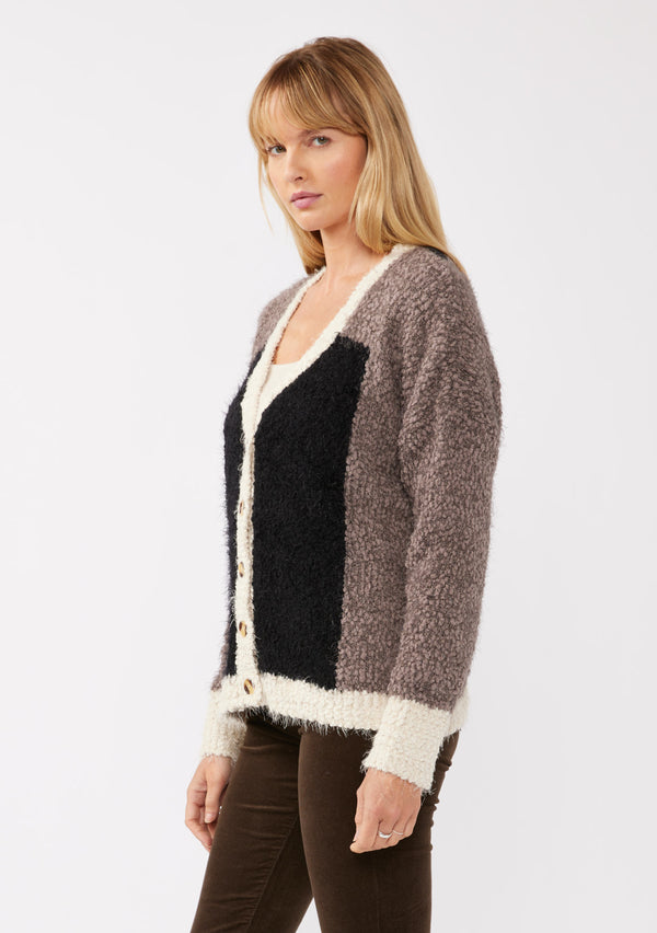 [Color: Vanilla Black] A side facing image of a blonde model wearing an ultra warm color block cardigan in a soft fuzzy popcorn texture. Featuring a classic tortoiseshell button up front, a flattering v neckline, and a contrast trim. This fuzzy cardigan is perfect for layering during the fall season. 