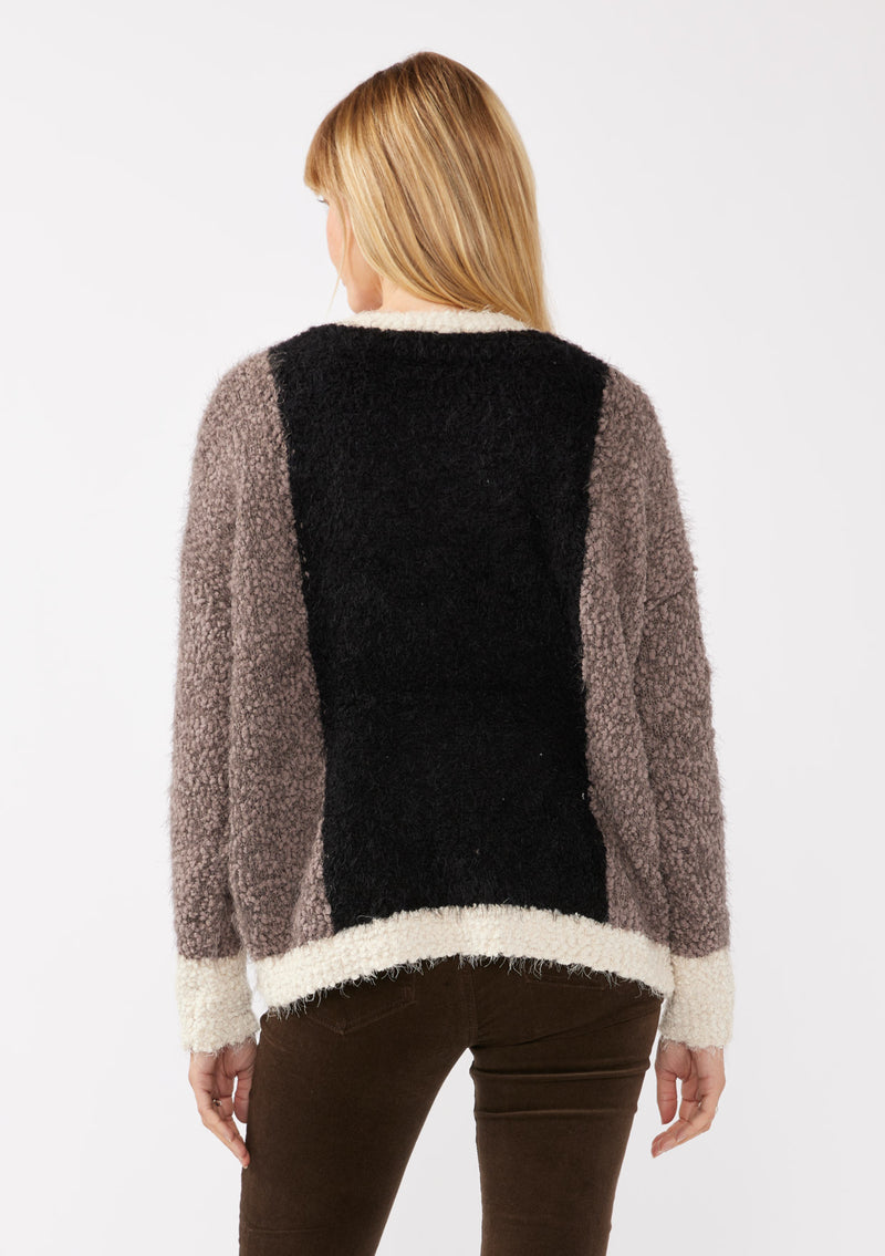 [Color: Vanilla Black] A back facing image of a blonde model wearing an ultra warm color block cardigan in a soft fuzzy popcorn texture. Featuring a classic tortoiseshell button up front, a flattering v neckline, and a contrast trim. This fuzzy cardigan is perfect for layering during the fall season. 