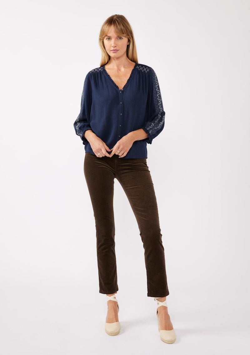 [Color: Navy] A full body front facing image of a blonde model wearing an embroidered, navy blue blouse with a button front, ruffle trimmed v-neckline, 3/4 sleeves, and elastic wrist cuffs. Paired with brown corduroy bottoms for a laid back fall look. 