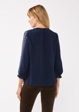 [Color: Navy] A back facing image of a blonde model wearing an embroidered, navy blue blouse with a button front, ruffle trimmed v-neckline, 3/4 sleeves, and elastic wrist cuffs. Paired with brown corduroy bottoms for a laid back fall look. 