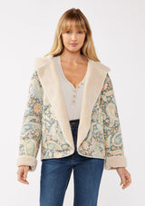 [Color: Midnight/Blush] A front facing image of a blonde model wearing a green paisley and floral print jacket with a sherpa lining. A boho statement jacket with long sleeves, patch pockets, a hoodie, and a cozy draped silhouette for warmth and comfort. Styled with denim for a casual fall or winter look. 