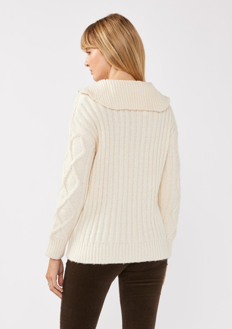 [Color: Natural] A back facing image of a blonde model wearing a cozy cable knit pullover sweater in off white. This casual fall knit features a front half zipper front, long sleeves, and a rib trim hem and cuffs. 