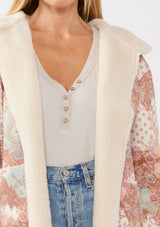 [Color: Brick/Cream] A detail image of a blonde model wearing a popular floral jacket with sherpa lining. This cozy fall and winter jacket features long sleeves, patch pockets, and a hoodie, draped for all-day comfort and warmth. Ideal for colder temperatures.