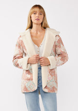 [Color: Brick/Cream] A front facing image of a blonde model wearing a popular floral jacket with sherpa lining. This cozy fall and winter jacket features long sleeves, patch pockets, and a hoodie, draped for all-day comfort and warmth. Ideal for colder temperatures.