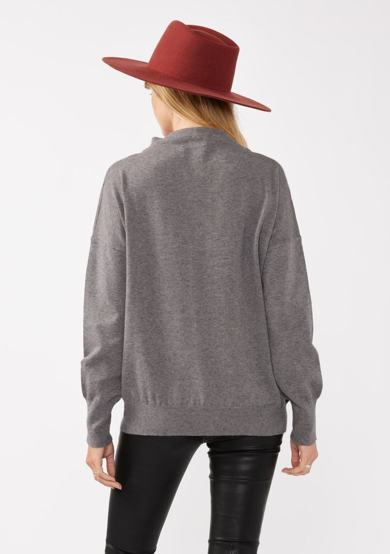 [Color: Heather Charcoal] A back facing image of a blonde model wearing a grey cozy lightweight pullover with a mock neckline. Complete with long sleeves, dropped shoulders, and a snugged ribbed trim. Perfect for layering or styling on its own for a relaxed, laid-back fall look. 