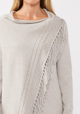 [Color: Heather Grey] A detail image of a blonde model wearing a grey fringed cardigan with an asymmetrical wrap design. The cardigan features hidden shoulder buttons for a wrap-front style, long sleeves, and intricate cable knit detailing.