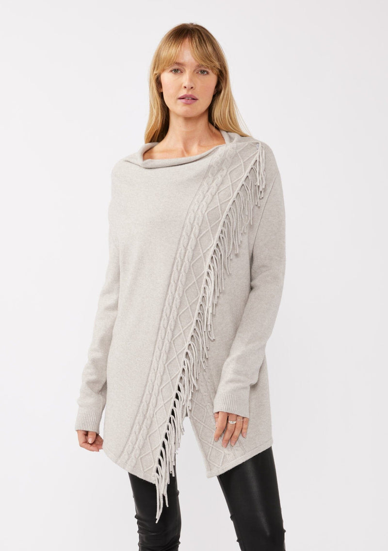 [Color: Heather Grey] A front-facing image of a blonde model wearing a grey fringed cardigan with an asymmetrical wrap design. The cardigan features hidden shoulder buttons for a wrap-front style, long sleeves, and intricate cable knit detailing.