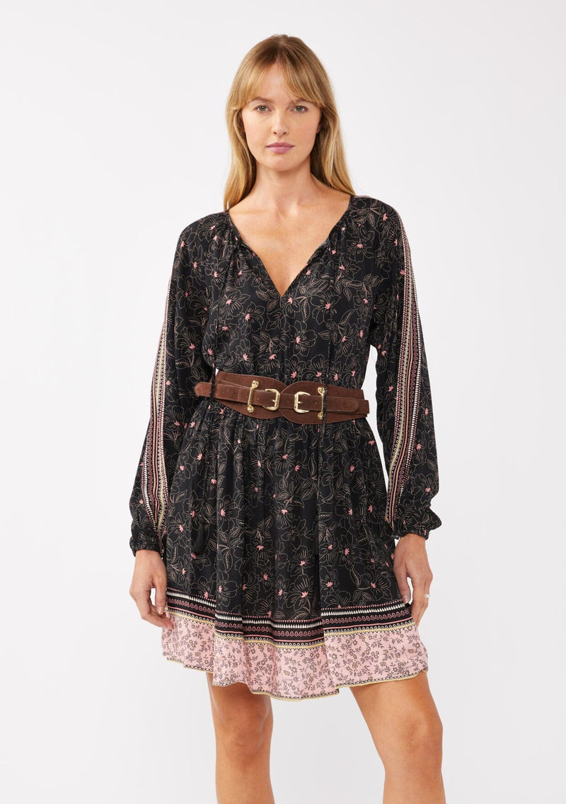 [Color: Black/Rose] A model wearing a classic black bohemian mini dress in a pink floral border print. With a loose, relaxed silhouette, long sleeves, and a split v neckline with tassels.