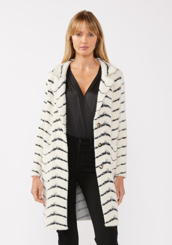 [Color: Cream/Black] A front facing image of a blonde model wearing a soft and fuzzy sweater coat in a white and black chevron design. With a snap button front, side pockets, and a classic notched lapel.