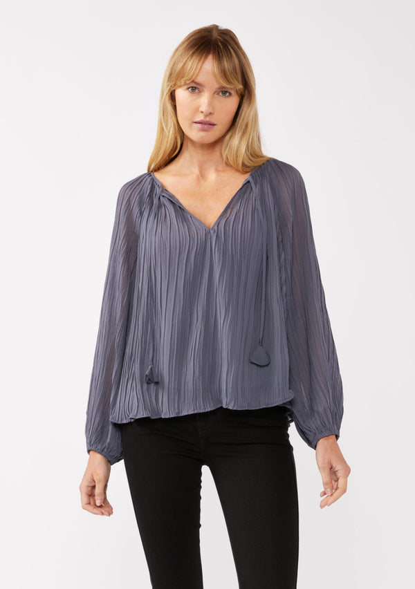 [Color: Slate Blue] A front facing image of a blonde model wearing a blue pleated chiffon blouse. Featuring a split v-neckline with tie detail, long sleeves, and elastic cuffs. A flowy, relaxed top for the office or special occasions. 