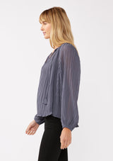 [Color: Slate Blue] A side facing image of a blonde model wearing a blue pleated chiffon blouse. Featuring a split v-neckline with tie detail, long sleeves, and elastic cuffs. A flowy, relaxed top for the office or special occasions. 