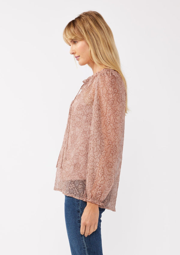 [Color: Mauve] A side facing image of a blonde model wearing a crinkled sheer chiffon blouse with a floral pattern. This relaxed fit blouse features a double tie neck detail, long sleeves with ruffled elastic cuffs, and a detachable cami. 