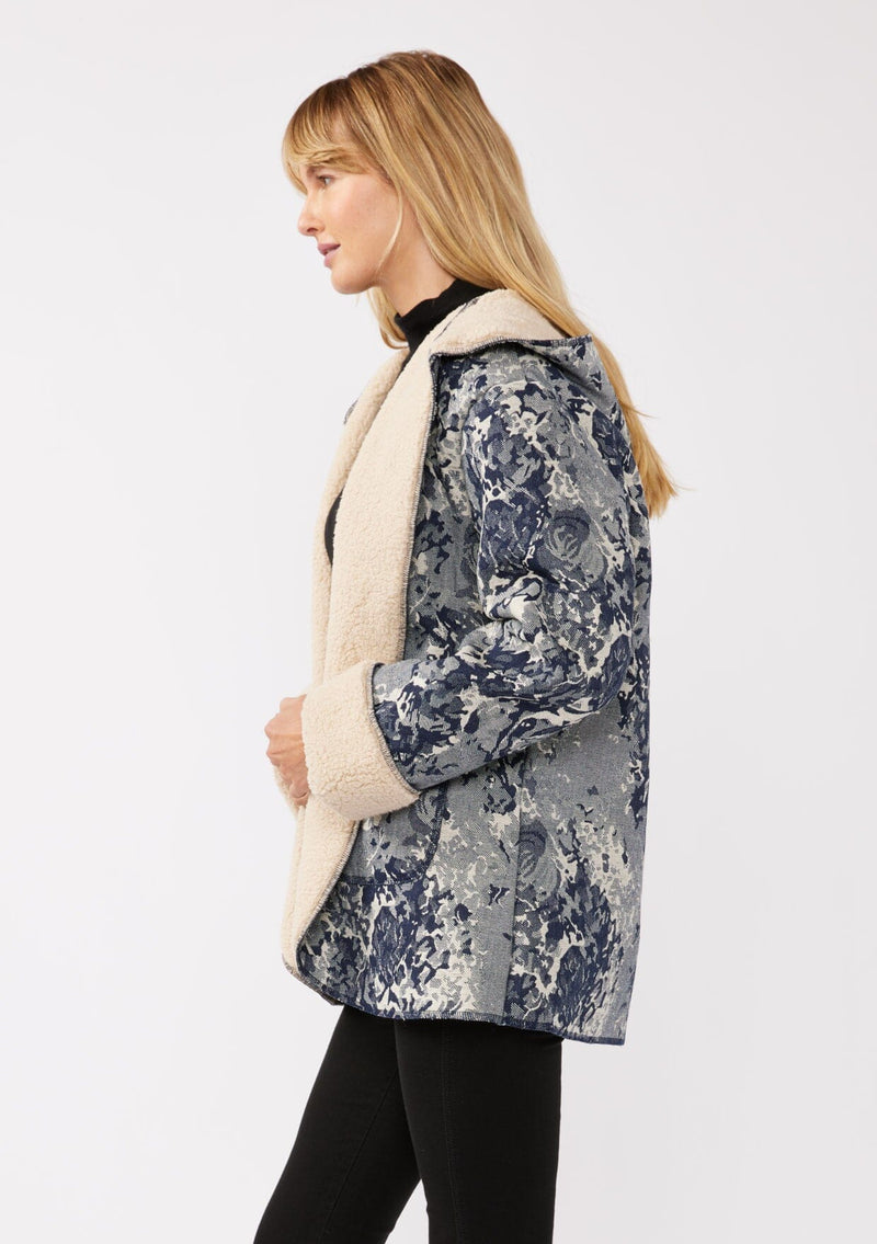 [Color: Denim Blue] A side-facing image of a blonde model wearing a denim floral jacket with a sherpa lining. The jacket features a cozy shawl collar, open front, patch pockets, long sleeves, and fold-over cuffs with exposed sherpa.