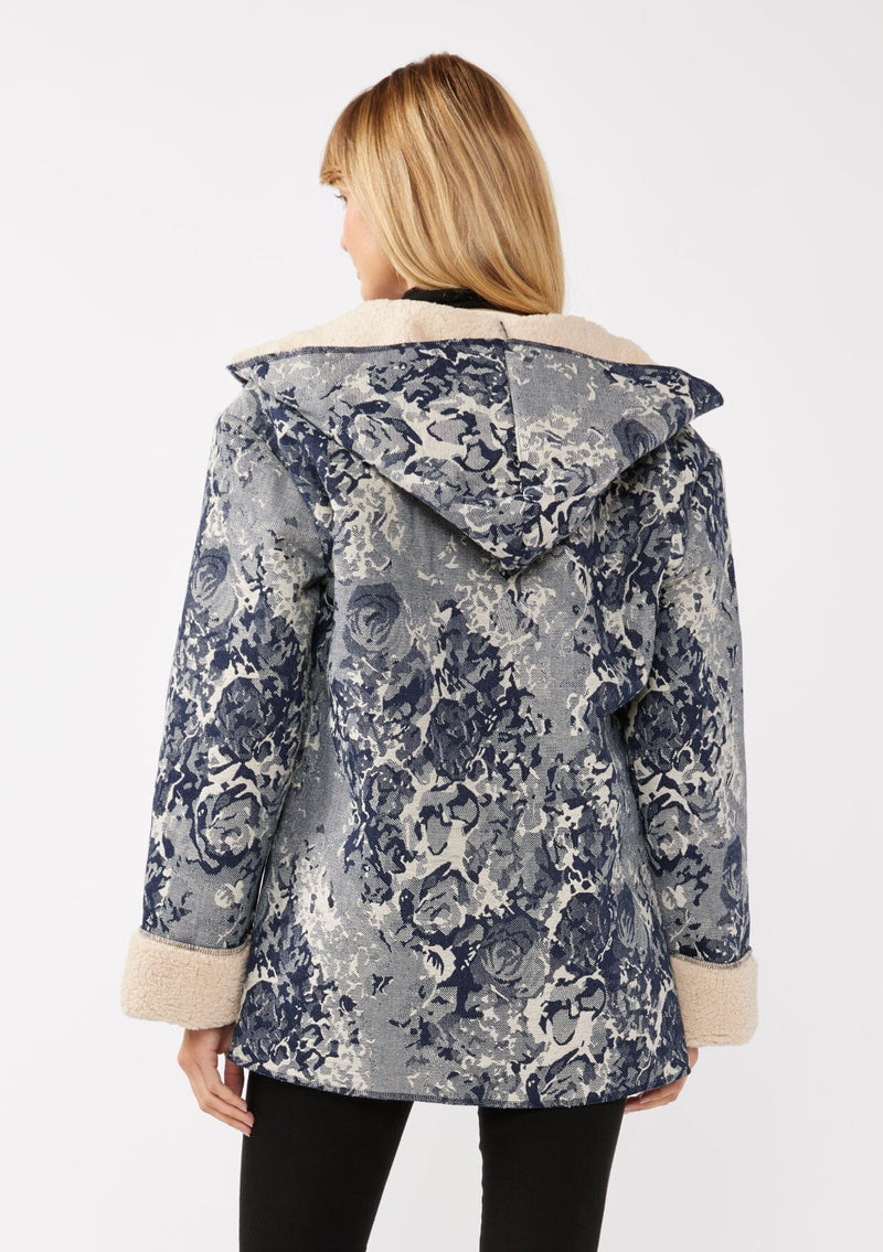 [Color: Denim Blue] A back-facing image of a blonde model wearing a denim floral jacket with a sherpa lining. The jacket features a cozy shawl collar, open front, patch pockets, long sleeves, and fold-over cuffs with exposed sherpa.