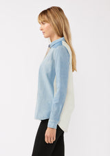 [Color: Denim] A side facing image of a blond model wearing a unique color block button down shirt in denim blue. Featuring a classic button front, long sleeves, button wrist closure, and collared neckline. Perfect for fall styling. 